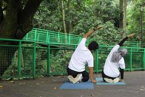 vista posteriore delle coppie musulmane asiatiche che fanno pratica yoga sul tappetino yoga nel parco verde. foto