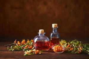 bottiglia di vetro con bacche di olio di olivello spinoso e rami di olivello spinoso su fondo di legno