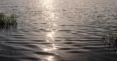 bagliore di luce del sole su il superficie di il lago acqua con piccolo onde foto