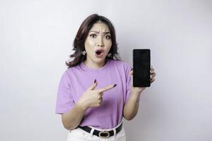 sorpreso donna indossare un' lilla viola camicia mostrando copia spazio su sua smartphone, isolato di un' bianca sfondo foto