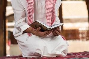 l'uomo musulmano in Dishdasha sta leggendo il Corano foto