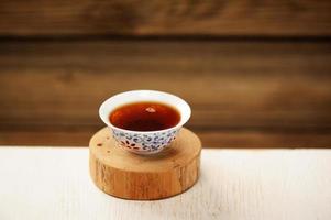 tè nero puerh in una ciotola bianca su supporto in legno foto