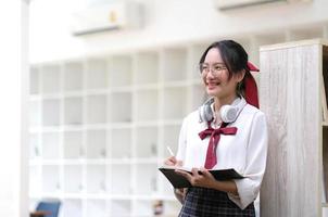 giovane donna asiatica d'affari è in piedi a una scrivania e prende appunti su un taccuino. il concetto di educazione e tecnologia. foto