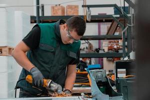 interno di una fabbrica di ingegneria dell'industria pesante con un lavoratore industriale che utilizza una smerigliatrice angolare e taglia un tubo di metallo. appaltatore in uniforme di sicurezza e elmetto per la produzione di strutture metalliche. foto