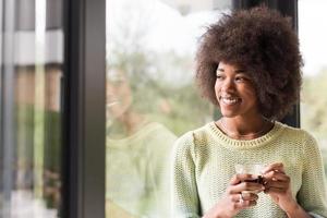 africano americano donna potabile caffè guardare su il finestra foto