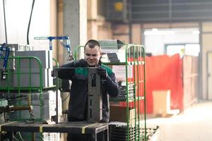 un' in uniforme lavoratore Lavorando nel un' moderno metallo produzione e in lavorazione fabbrica assembla parti di un' nuovo macchina su il suo scrivania foto