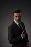 ritratto di un' elegante elegante anziano uomo d'affari con un' barba e casuale attività commerciale Abiti nel foto studio isolato su buio sfondo Esprimere a gesti con mani