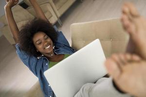 africano americano donne a casa nel il sedia utilizzando un' il computer portatile foto