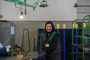 un' ritratto di un' donna nel uniforme trasporto un' pezzo di metallo e preparazione esso per il finale parte di produzione foto