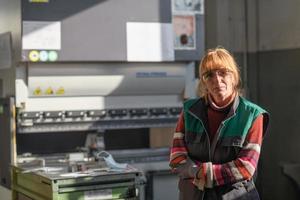 ritratto di un' donna in piedi nel davanti di un' cnc macchina nel occhiali e Lavorando nel un' moderno metallo produzione e in lavorazione fabbrica foto