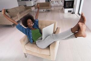 africano americano donne a casa nel il sedia utilizzando un' il computer portatile foto