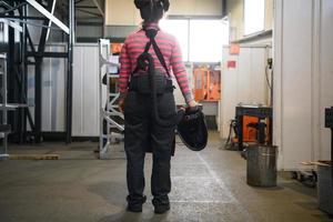 un' femmina saldatore preparazione per un' Lavorando giorno nel il metallo in lavorazione industria indossa un' maschera su sua viso dovuto per il coronavirus pandemia foto