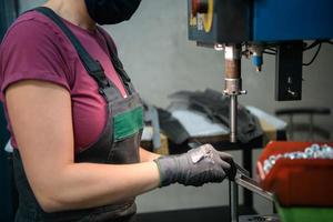 donna indossare maschera dovuto per coronavirus pandemia mentre Lavorando nel moderno metallo industria e utilizzando trapano foto