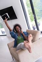 africano americano donna a casa nel sedia con tavoletta e testa telefoni foto