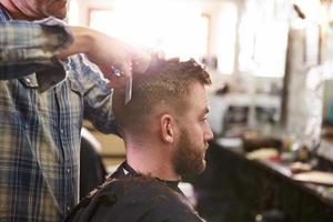 barbiere maschio che dà taglio di capelli del cliente in negozio foto
