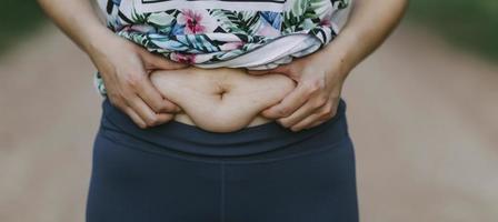 bella donna grassa con metro a nastro usa la mano per spremere il grasso in eccesso che è isolato su uno sfondo bianco. vuole perdere peso, il concetto di chirurgia e abbattere il grasso sotto il foto