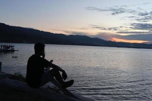 silhouette di un' giovane uomo in piedi di il lago godendo il tramonto. tranquillo, calmo atmosfera nel natura foto