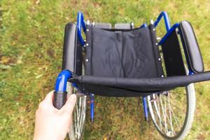 mano che tiene una sedia a rotelle vuota nel parco dell'ospedale in attesa di servizi per i pazienti. sedia a rotelle per persone con disabilità parcheggiate all'aperto. accessibile a persone con disabilità. concetto medico sanitario. foto