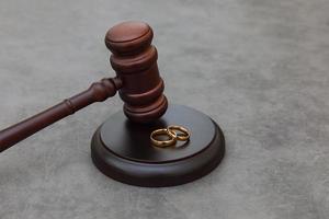 legge tema. giudice martelletto nozze anelli su calcestruzzo pietra grigio sfondo. divorzio procedimento. maglio di giudice decidere su matrimonio divorzio, coniugale accordo, legalità di divorzio. foto