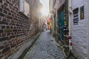 vecchio bicicletta su il bordo di un vecchio stretto marciapiede strada. tramonto, bicicletta e mattone muri nel Bruges, Belgio. foto