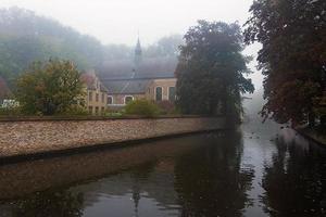 begijnhof, Bruges. nebbioso autunno mattina, foschia al di sopra di il acqua di canale e riflessi di alberi e antico belga case nel acque minerarie parco nel brugge foto