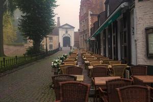 presto autunno mattina nel begijnhof, Brugge, Belgio. nebbia al di sopra di il ciottolo marciapiede, vuoto ristorante sedie e tavoli. abbandono e fantasma poco medievale cittadina concetto. foto