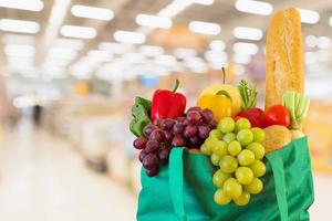 frutta e verdura fresca in una borsa della spesa verde riutilizzabile con un supermercato sfocato sfondo sfocato con luce bokeh foto