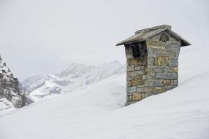 tetto di casa di montagna con camino fumante sullo sfondo bianco profondo della neve foto