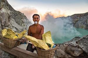 Giava, Indonesia - agosto, 9, 2016 - minatori trasporto zolfo a partire dal ijen vulcano blu fiamme a notte foto