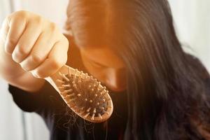 posteriore Visualizza giovane donna preoccupato di capelli perdita problema, ormonale squilibrio, fatica concetto. molti capelli autunno dopo pettinatura nel capelli spazzola nel mano. femmina districato sua capelli con un' pettine, Salute cura foto