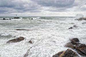 mare nel tempesta su rocce di italiano villaggio foto