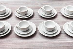 parecchi bianca tazze e piattini su grigio Marrone tavolo foto