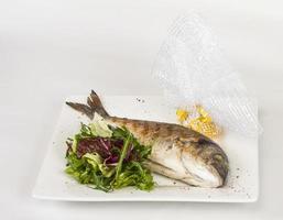 pesce Dorada con insalata sul piatto bianco. girato in studio foto