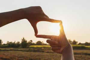 primo piano di una mano che incornicia il tramonto foto