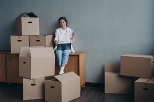 femmina con scatola di cartone scatole ricerca in movimento azienda a il computer portatile per trasferimento. mezzi di trasporto servizio foto