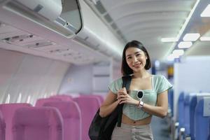 ritratto di un' donna trasporta un' valigia al di sopra di sua spalla mentre in piedi nel un' passeggeri su un' aereo. foto
