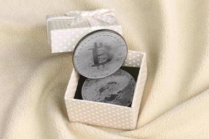 il argento bitcoin bugie nel un' piccolo arancia regalo scatola con un' piccolo arco su un' coperta fatto di morbido e soffice leggero arancia vello tessuto con un' grande numero di sollievo pieghe foto