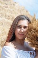 giovane donna seduta su pagliaio nel raccolto campo Tenere Grano mazzo foto