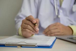 medico uniforme Lavorando mano Tenere penna appunti documento medicina professione carta ospedale Salute cura su scrivania. foto