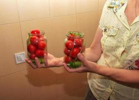 il processi di preservare pomodori per il inverno. femmina mani pila maturo rosso succoso pomodori nel bicchiere barattoli. foto