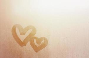 coppia di astratto sfocato amore cuore simbolo disegnato di mano su il bagnato finestra bicchiere con luce del sole sfondo. modello per San Valentino giorno cartoline foto