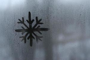 il Immagine di il fiocco di neve è disegnato con un' dito su il superficie di un' appannato bicchiere finestra. gelido tempo metereologico foto