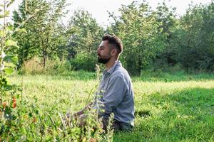 ritratto di giovane bello sorridente europeo uomo nel casuale capi di abbigliamento seduta su un' erba nel estate parco. foto