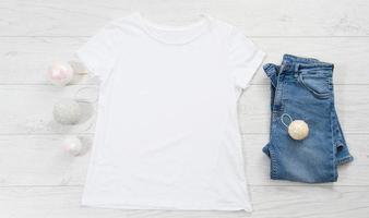 vicino su bianca vuoto modello t camicia con copia spazio e Natale vacanza concetto. superiore Visualizza modello maglietta e jeans su bianca di legno sfondo. contento nuovo anno decorazioni Accessori. natale attrezzatura foto