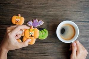 mano Tenere caffè tazza durante mangiare divertente Halloween biscotti. contento Halloween giorno, trucco o minaccia, Ciao ottobre, autunno autunno, tradizionale, festa e vacanza concetto foto