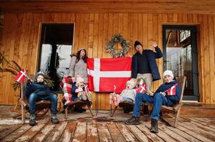 famiglia con bandiere danimarca vicino alla loro casa di legno. viaggiare nei paesi scandinavi. i danesi più felici. foto