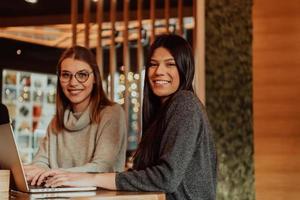 Due giovane attività commerciale donne seduta a tavolo nel bar. ragazza Spettacoli collega informazione su il computer portatile schermo. ragazza utilizzando smartphone, blogging. lavoro di squadra, attività commerciale incontro. foto