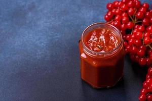 Viburnum frutta marmellata nel un' bicchiere vaso su un' buio calcestruzzo sfondo foto