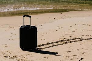 nero viaggio valigia su sabbioso spiaggia con turchese mare sfondo, estate vacanze concetto foto