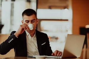 contento attività commerciale uomo seduta a caffetteria con il computer portatile e smartphone foto